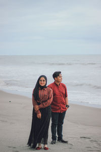 Full length of friends standing on beach against sky