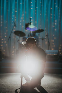 Man sitting on stage, photographer taking photos on stage, man in front of drum. 