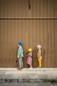 Children standing on footpath by brown wall