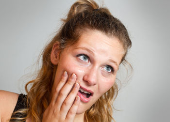 Close-up of young woman suffering from toothache against gray background