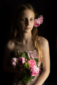 Portrait of young woman with bouquet of roses against black background