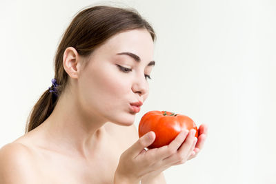 Close-up portrait of a young woman holding apple against white background