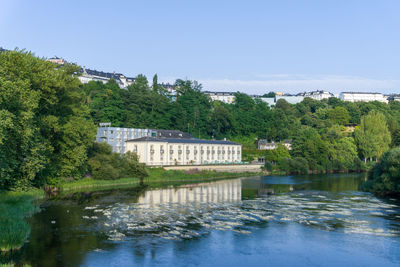 River by trees and buildings against sky