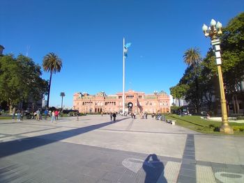 People walking on road with palm trees against clear blue sky