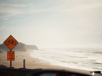 Close-up of road sign on beach against sky