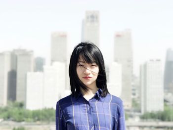 Portrait of young woman standing against cityscape