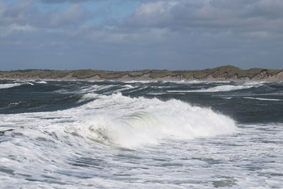 Waves rushing towards shore against sky