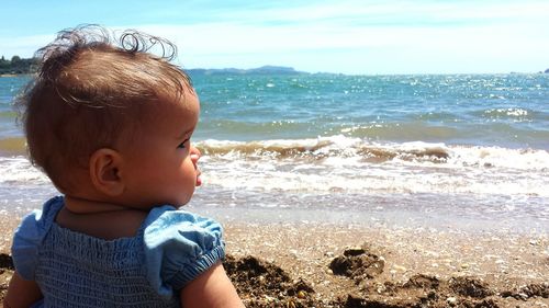 Rear view of baby girl sitting on shore at beach