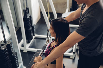 Midsection of instructor assisting woman in exercising at gym