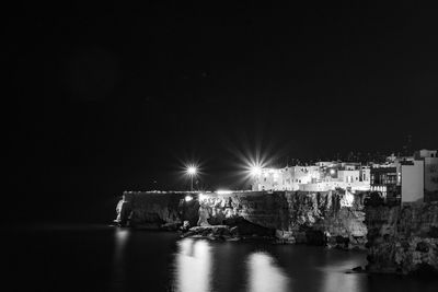 Illuminated built structure by sea against sky at night