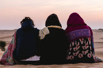 Rear view of friends sitting in desert during sunset