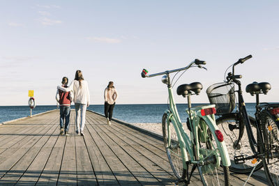 Rear view of friends walking on pier with bicycles in foreground at beach