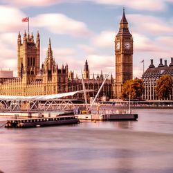 Pier on thames river by big ben and houses of parliament against sky