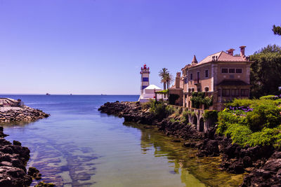 Buildings by sea against clear blue sky