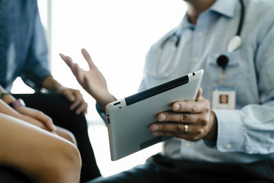 Cropped hand of pediatrician showing tablet computer to mother and daughter in medical examination room