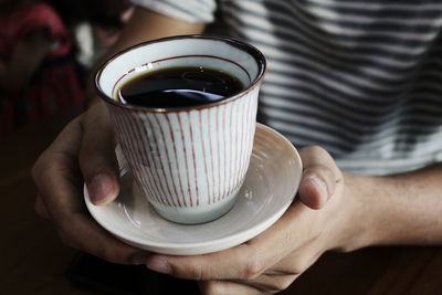 Close-up of hand holding coffee cup on table