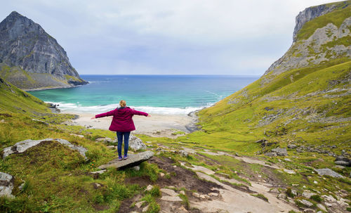 Rear view of man walking on cliff by sea against sky