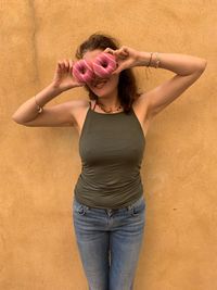 Woman holding doughnuts in front of eyes against wall