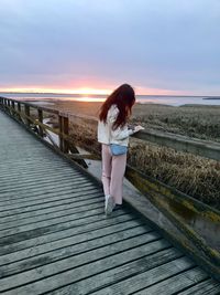 Woman standing on pier against sky during sunset