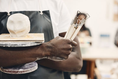 Midsection of young man holding work tools and molded clay in art class