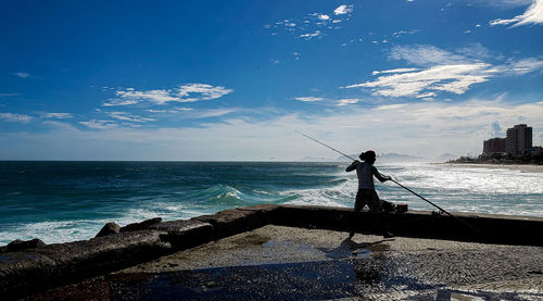 Man fishing in sea against sky