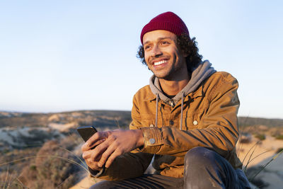 Young woman using mobile phone while sitting against sky