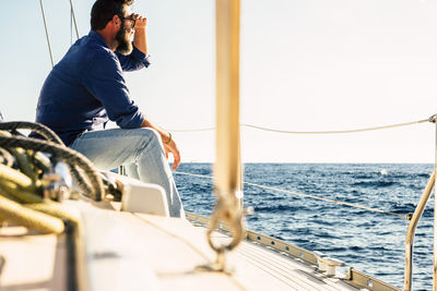 Rear view of man sitting on boat sailing in sea against sky