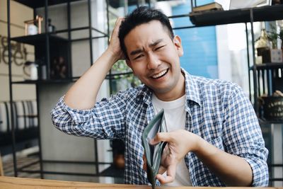 Portrait of man with hand in hair holding empty wallet