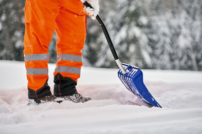 Low section of man with shovel standing on snow covered land