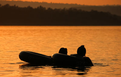 Silhouette people in sea against orange sky