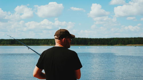 Rear view of man holding fishing rod while standing by lake