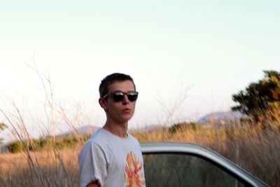 Portrait of young man standing on field against clear sky