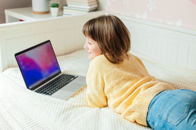 Smiling girl with laptop lying on bed at home