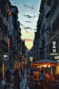 People walking at sidewalk cafe in city against sky