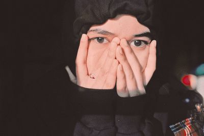 Close-up portrait of young woman with hands covering face against black background
