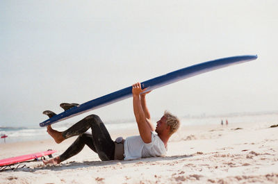 Full length of young man lying with surfboard at beach