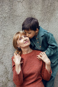 Child boy hugs his grandmother an elderly woman on the street against a gray wall