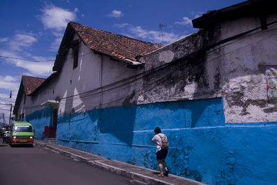 Rear view of man walking on road amidst buildings