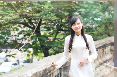 Portrait of young woman standing against trees