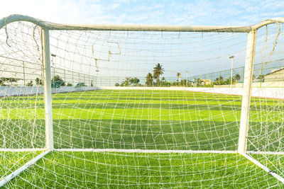 Scenic view of soccer field seen through net against sky