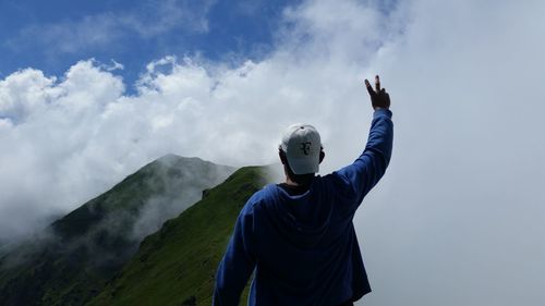 Rear view of man with arms raised against sky