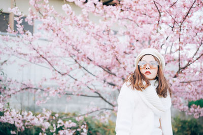 Young woman standing by cherry blossom tree