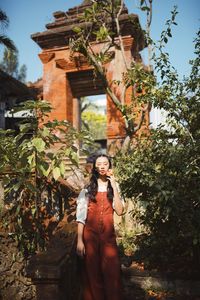 Beautiful young woman holding flower while standing against plant