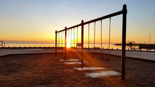 Empty swings at beach against sky during sunset