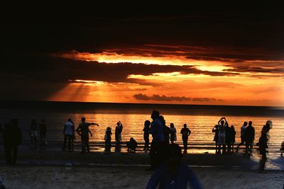 Silhouette people on beach against sky during sunset