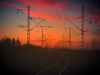 Silhouette electricity pylons by railroad tracks against romantic sky at sunset