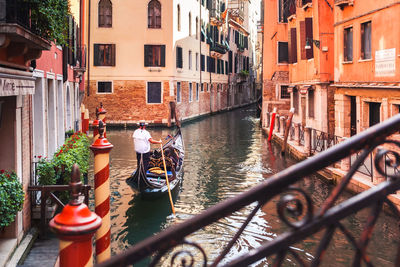 Venetian gondolier takes tourists on gondola ride down quiet narrow canal through venice