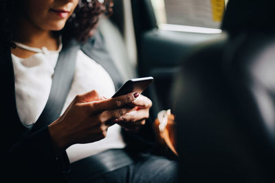 Midsection of businesswoman using smart phone while sitting in taxi