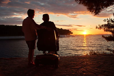 Rear view of people on beach against sky during sunset