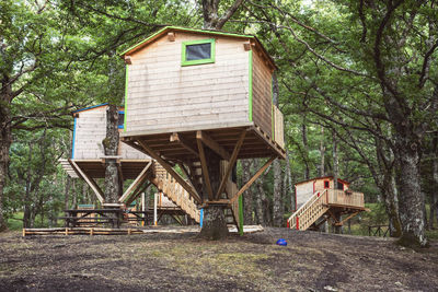 Wooden house amidst trees on field in forest